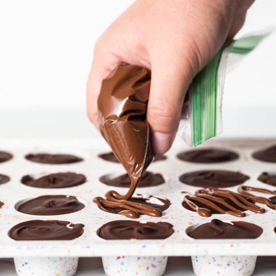 A person is dipping chocolate into a tray of cupcakes.