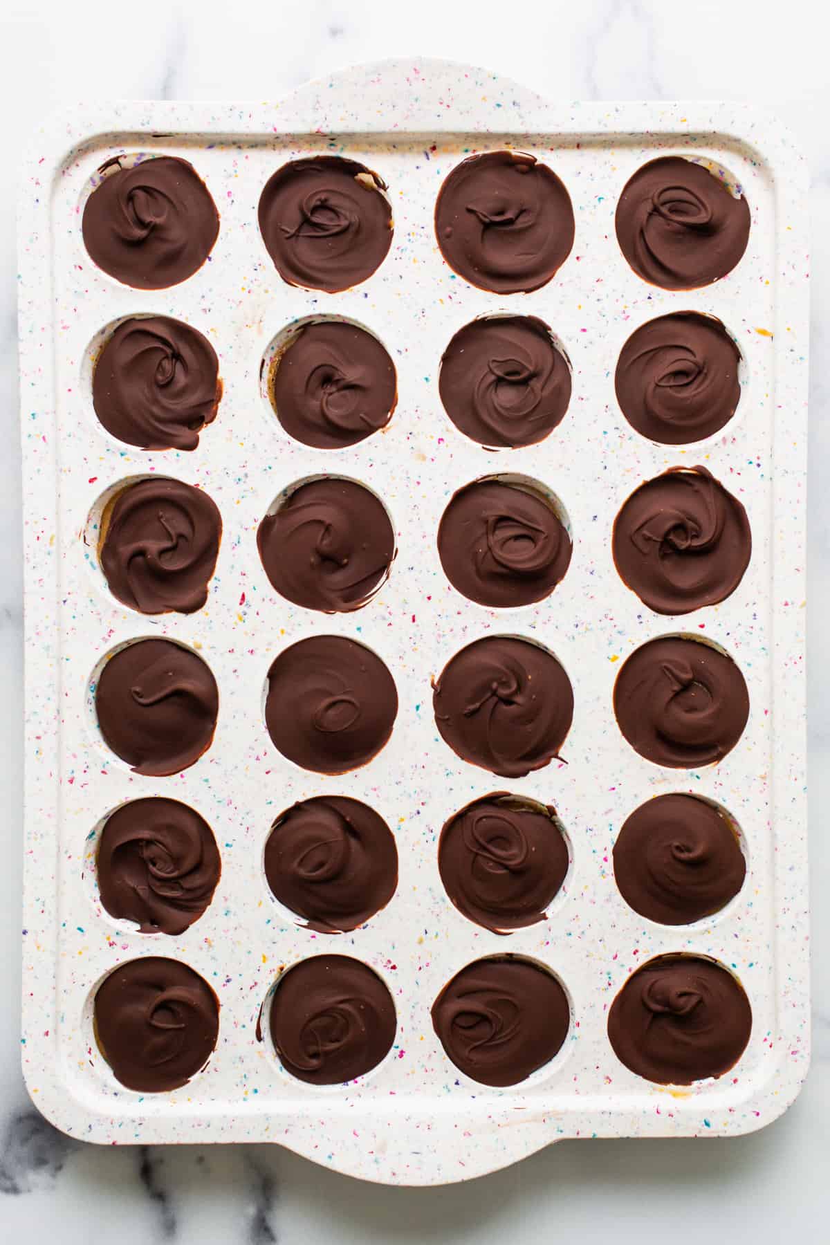 A tray of chocolate dipped cupcakes on a marble countertop.