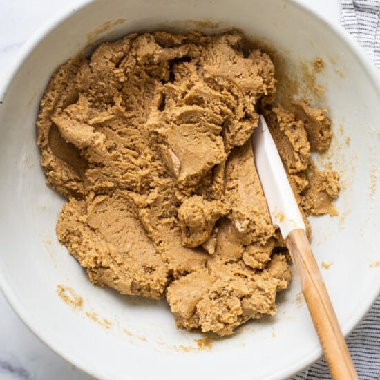 Peanut butter cookie dough in a bowl with a wooden spoon.