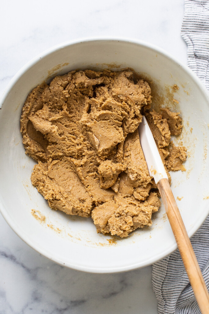 Peanut butter cookie dough in a bowl with a wooden spoon.