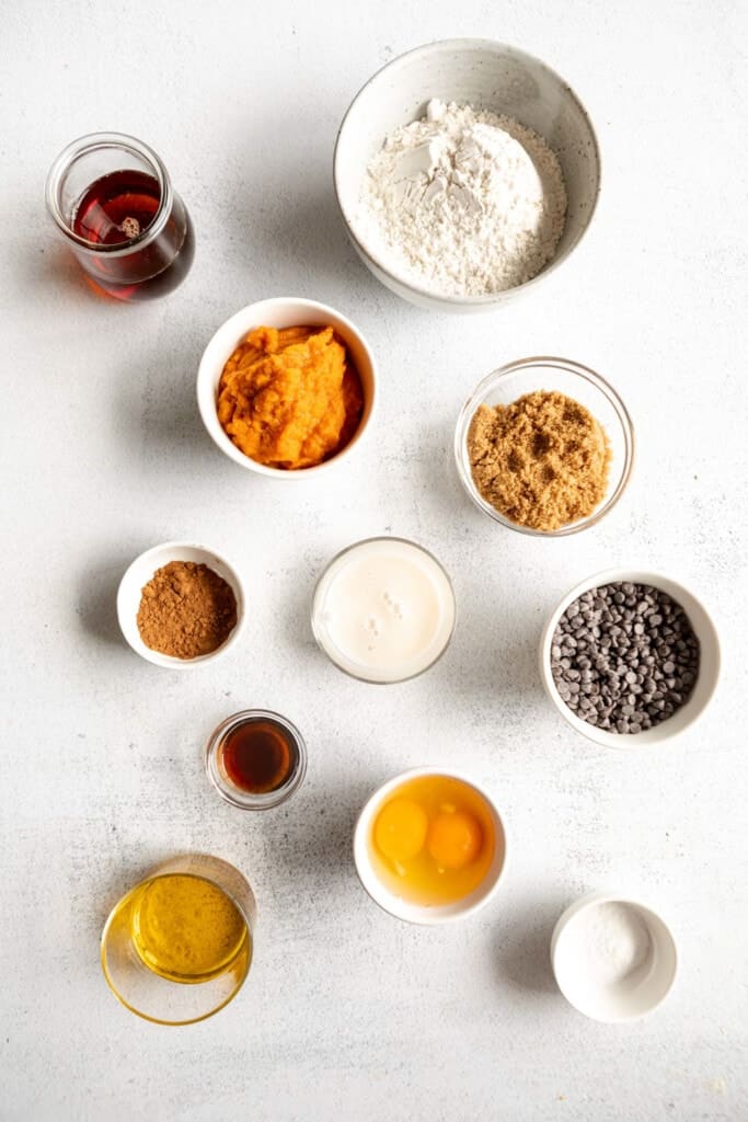 Ingredients for a pumpkin pie in bowls on a white surface.