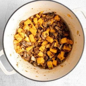 A white pot filled with squash and mushrooms.
