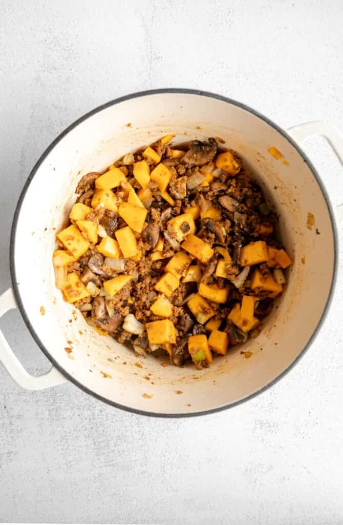 A white pot filled with squash and mushrooms.