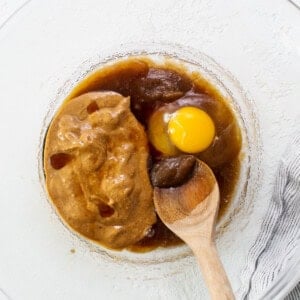 An egg in a glass bowl with a wooden spoon.