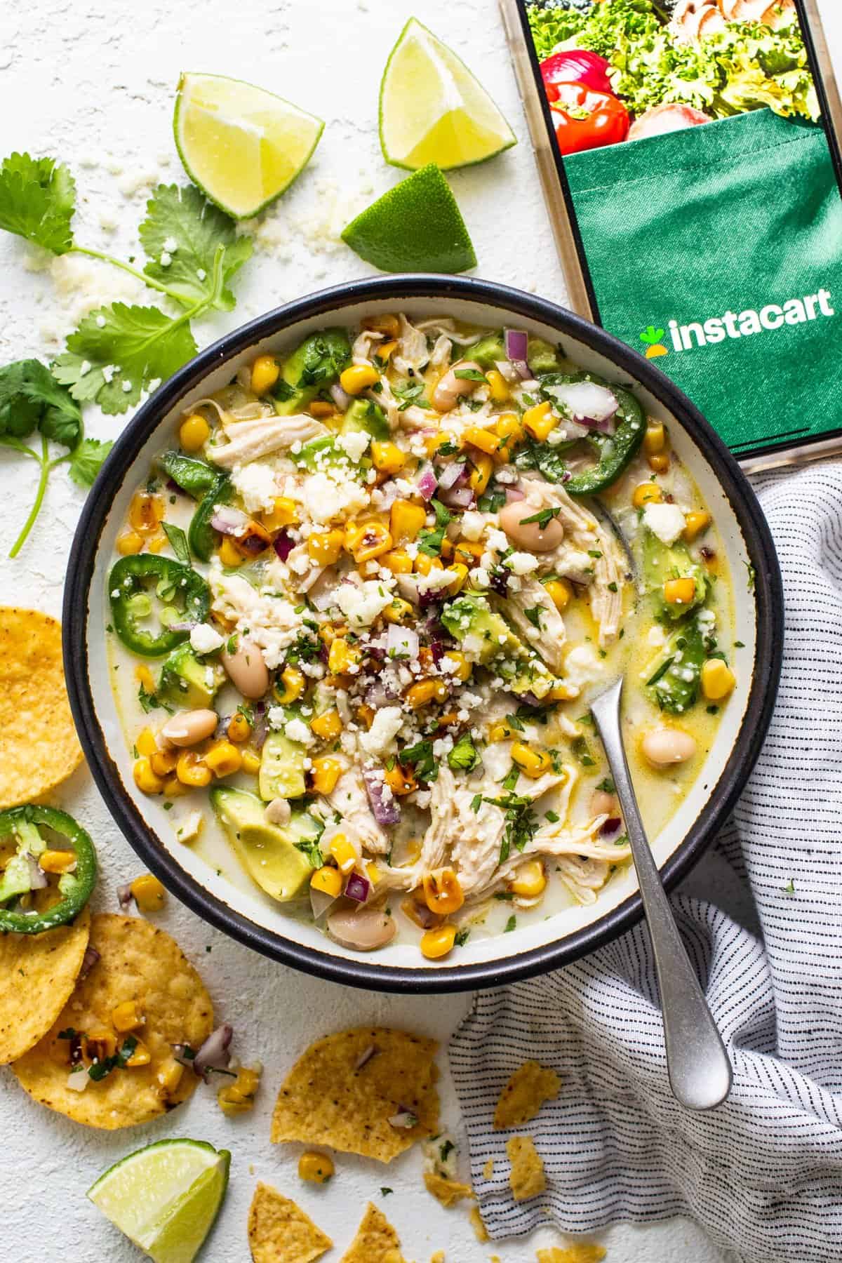 A bowl of chicken and corn soup with tortilla chips and limes.