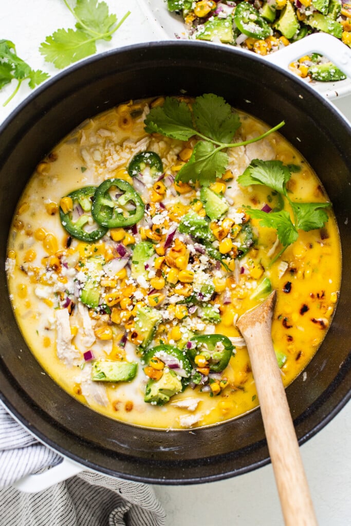 Chicken and corn soup in a pan with a wooden s،.