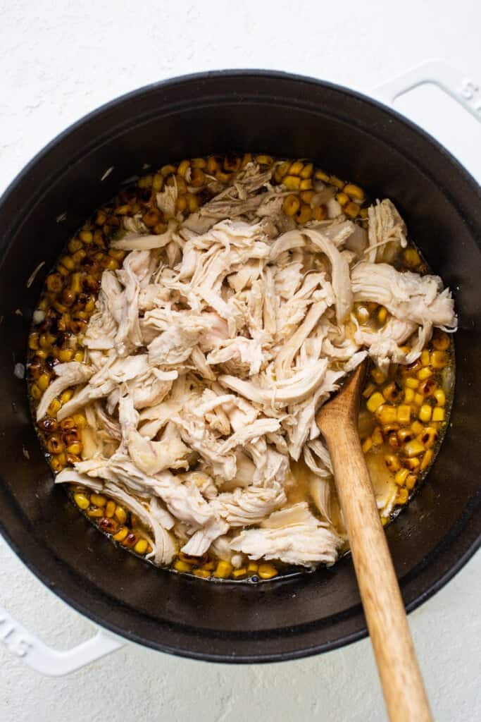 Chicken and corn in a pan with a wooden spoon.