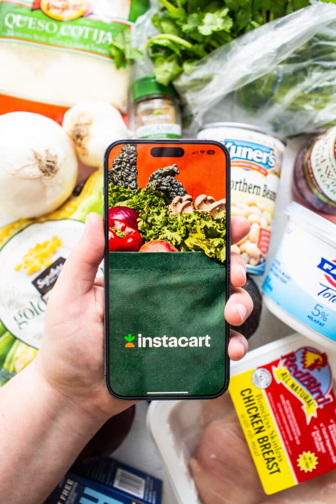 A person holding a phone up to a bag of groceries.