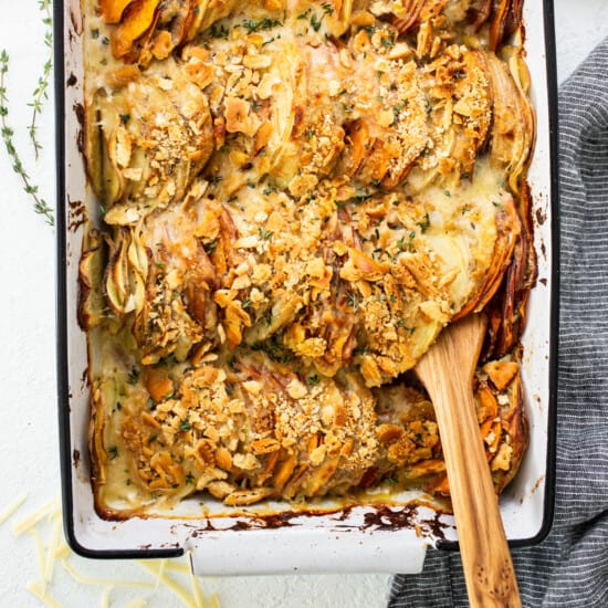 A baking dish filled with roasted potatoes and a wooden spoon.