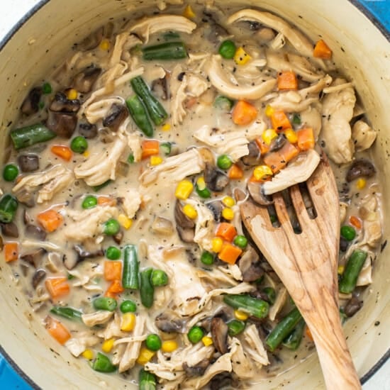 Chicken stew in a pot with vegetables and a wooden spoon.