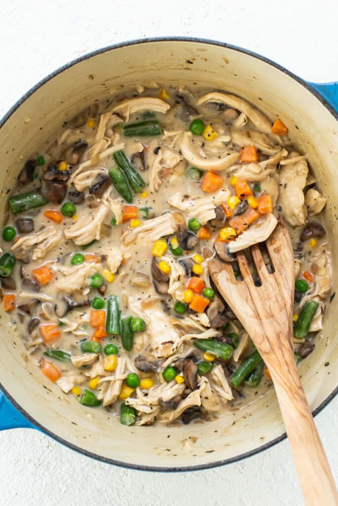 Chicken stew in a pot with vegetables and a wooden spoon.