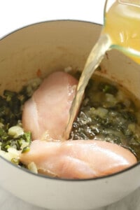 Chicken breasts being poured into a pan with green chili.