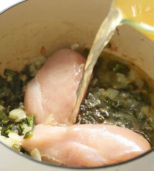 Chicken breasts being poured into a pan with green chili.