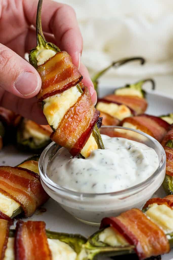 Bacon wrapped jalapenos with dipping sauce on a plate.