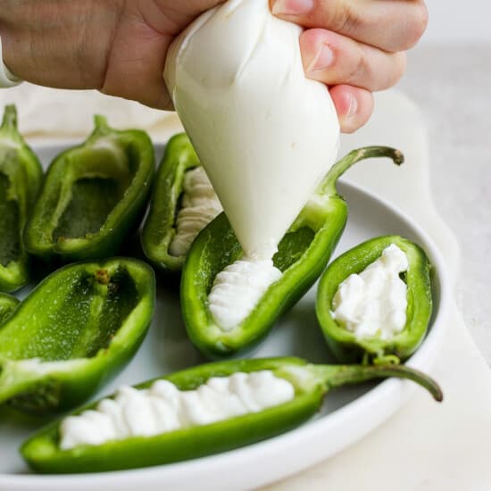 A person drizzling cream on green peppers on a plate.