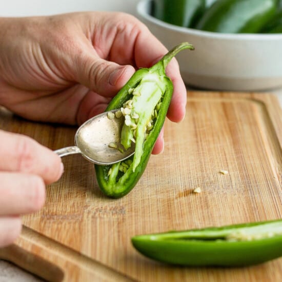 A person cutting a jalapeno pepper with a spoon.