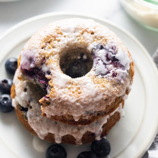 A stack of blueberry glazed donuts on a plate.