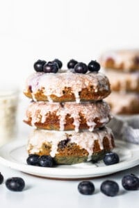 A stack of blueberry glazed donuts on a plate.