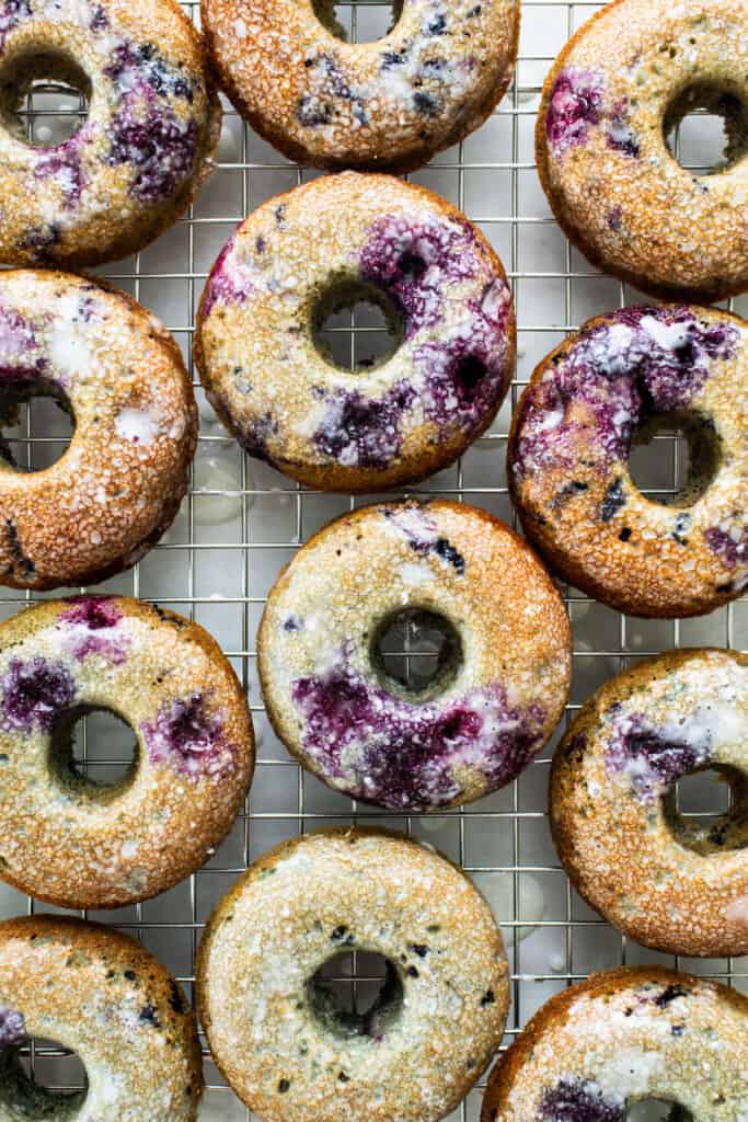 Blueberry donuts with powdered sugar on a cooling rack.