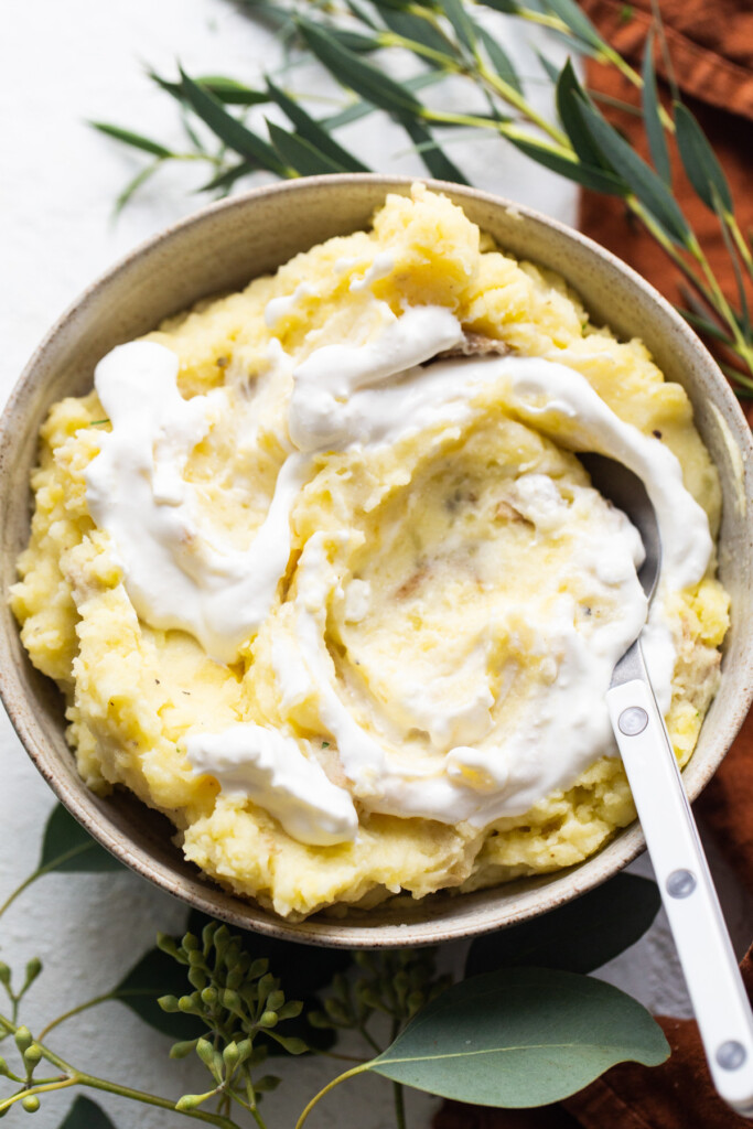 A bowl of mashed potatoes with whipped cream and eucalyptus leaves.