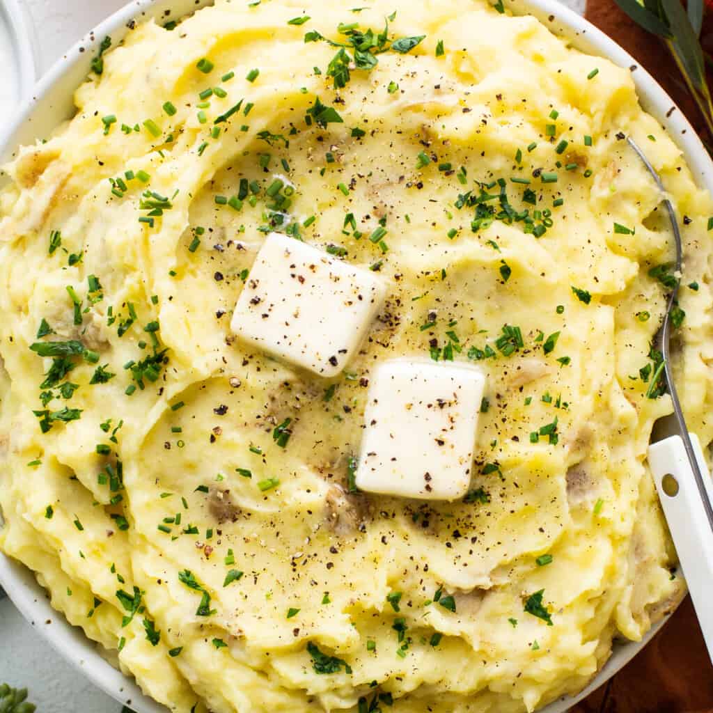 A vessel  of mashed potatoes with food  and herbs.