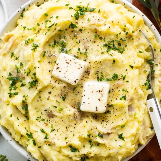 A bowl of mashed potatoes with cheese and herbs.