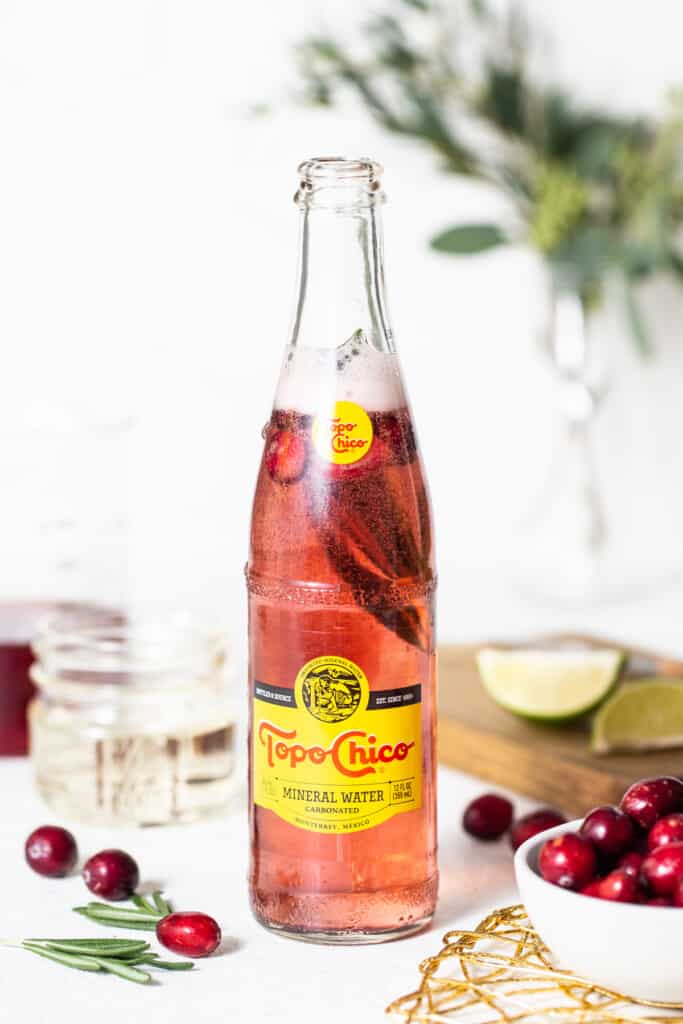 A bottle of cranberry juice with fresh cranberries and sprigs of rosemary.