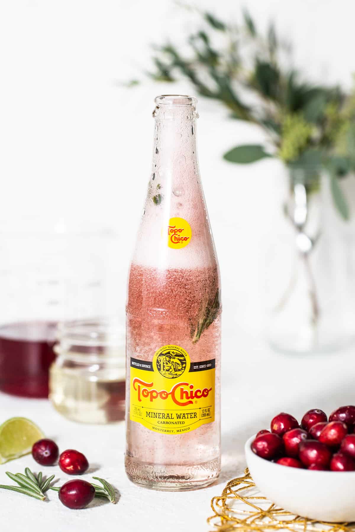 A bottle of cranberry gin with cranberries on a table.