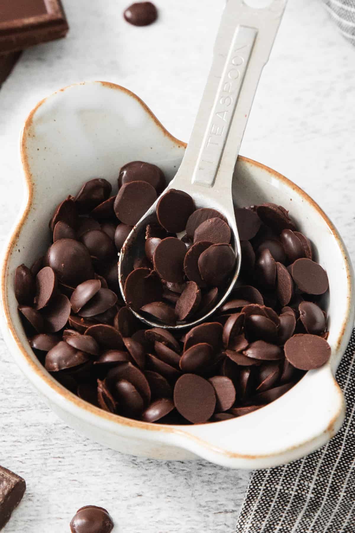 Chocolate chips in a white bowl with a spoon.