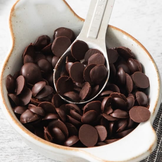Chocolate chips in a white bowl with a spoon.