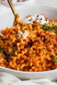 A bowl of pasta with meat sauce and sour cream.