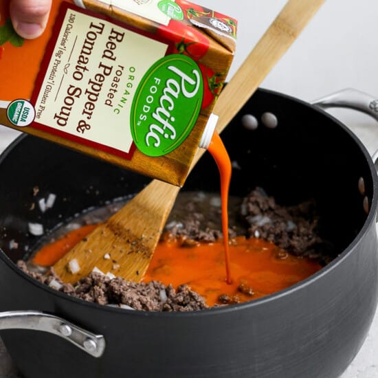 A person pouring a sauce into a pan.