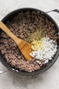 Ground beef and onions in a pan with a wooden spoon.