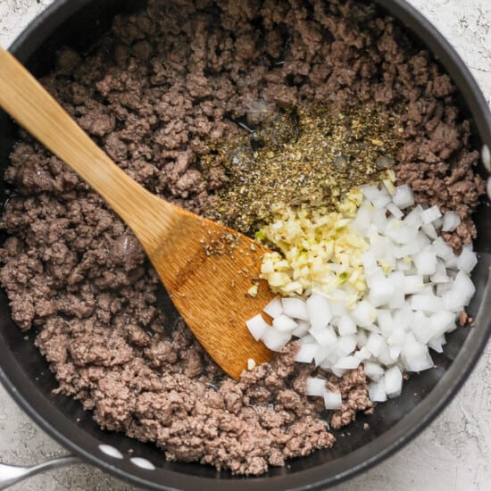 Ground beef and onions in a pan with a wooden spoon.