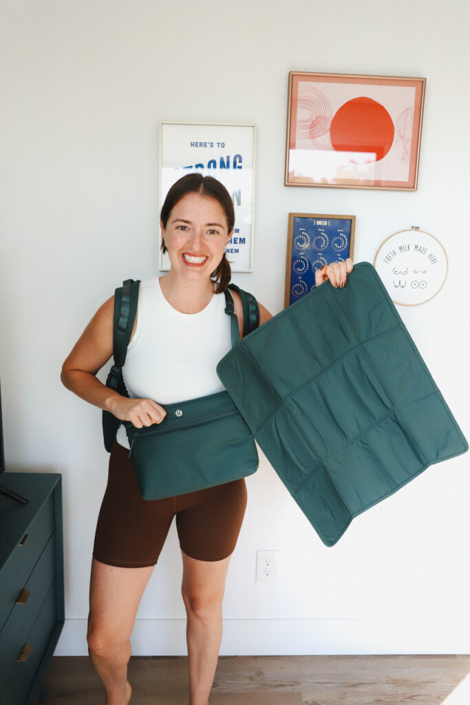 A woman holding a green bag in front of a wall.