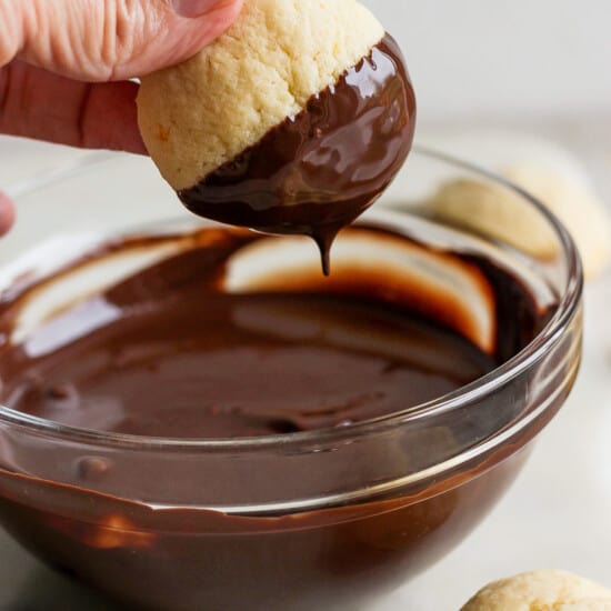 A person dipping a cookie into a bowl of chocolate.