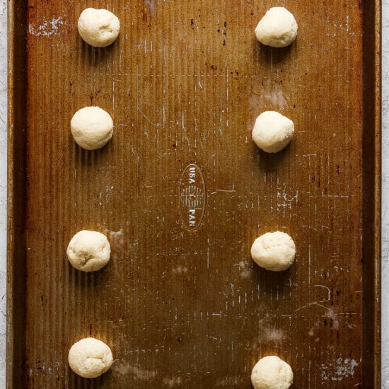 A baking sheet with a number of doughnuts on it.