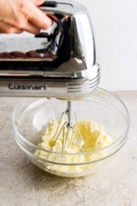 A person mixing butter in a bowl with a hand mixer.