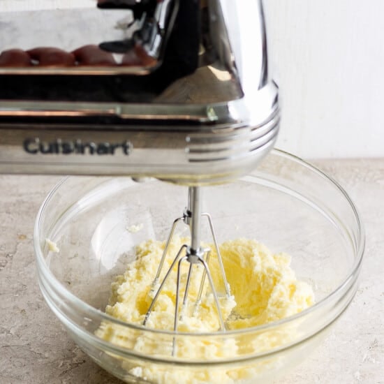 A person mixing butter in a bowl with a hand mixer.