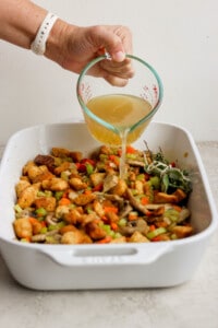 A person pouring a liquid over a dish of stuffing.