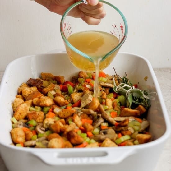 A person pouring a liquid over a dish of stuffing.