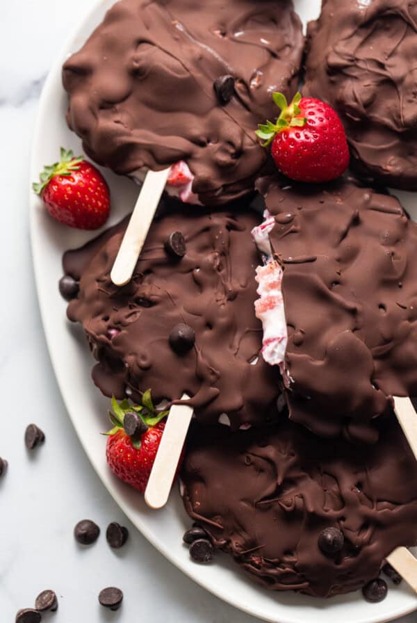 Chocolate covered strawberry popsicles on a plate.