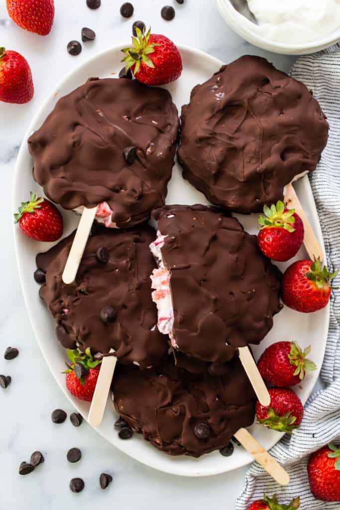 Chocolate covered strawberry popsicles on a plate.