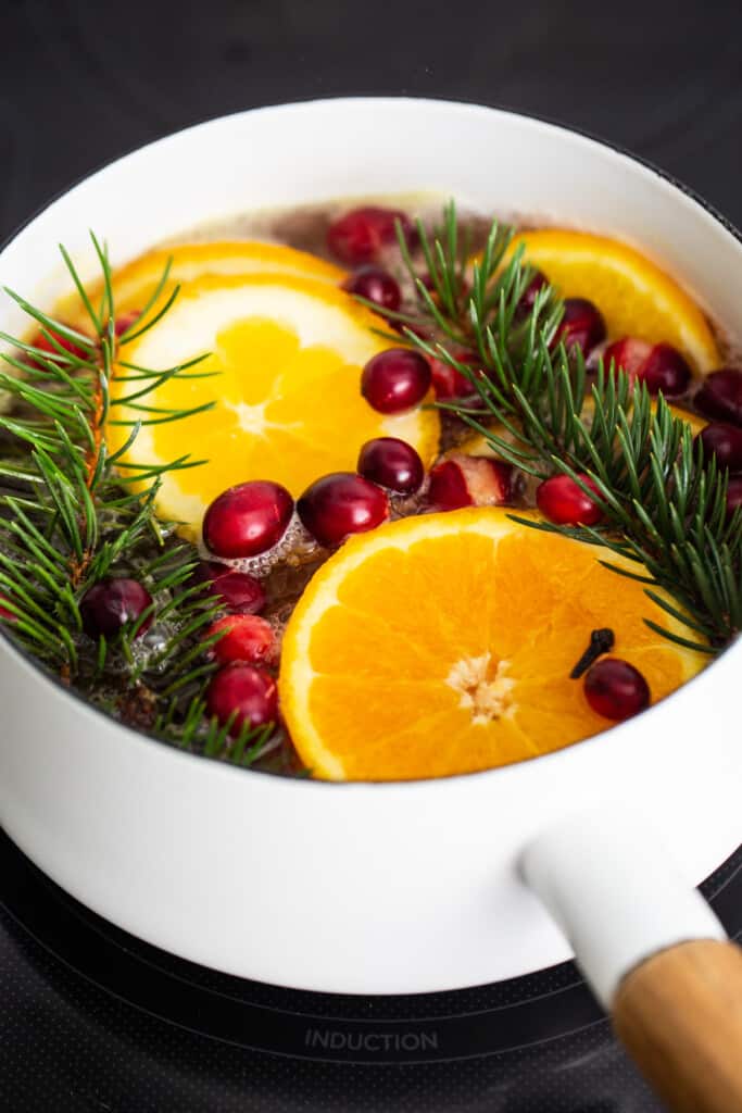 A pot of oranges, cranberries and fir sprigs.