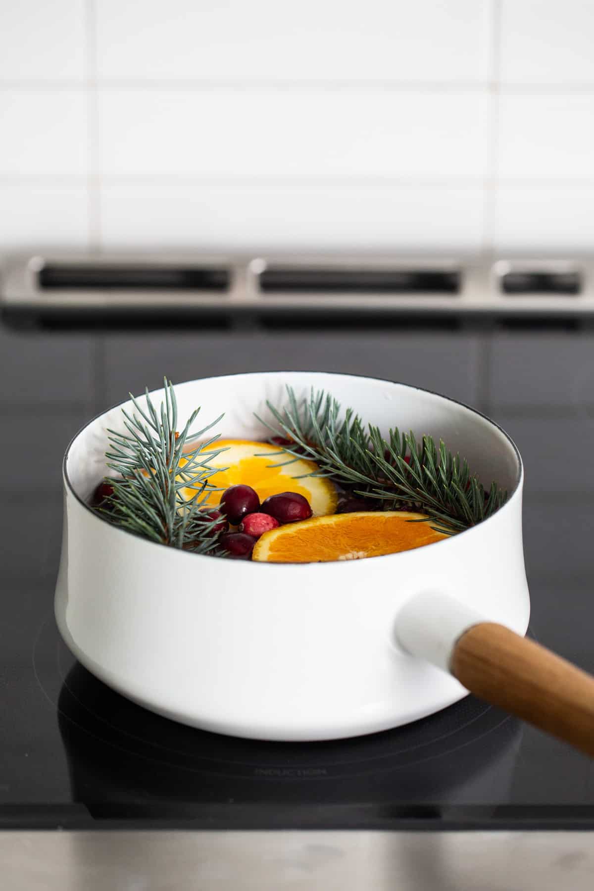 A white pan with oranges and pine needles on top of a stove.