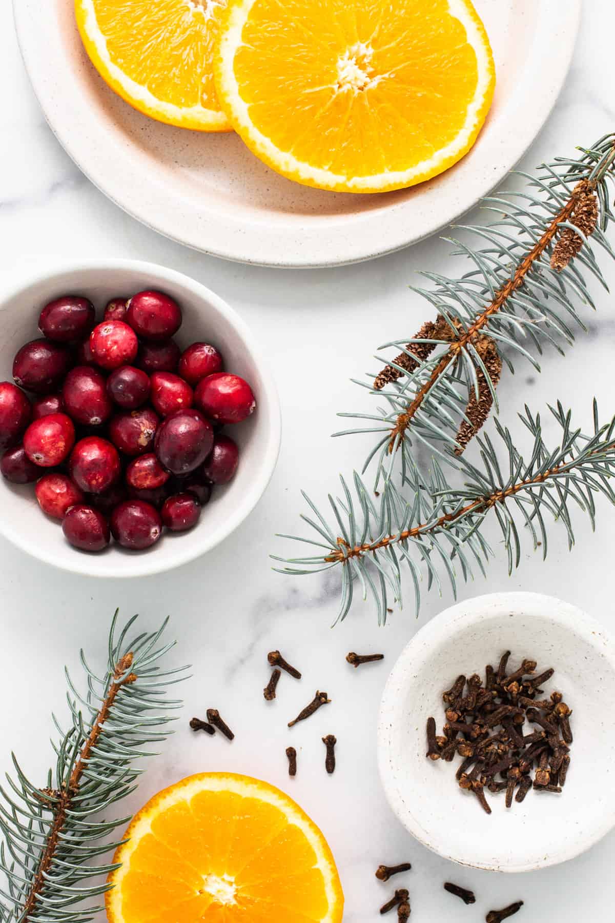 Cranberries, oranges and pine cones on a marble table.