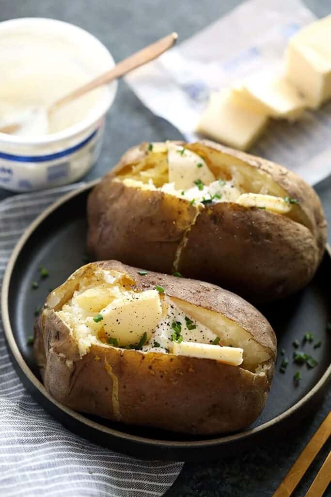 Two crock pot baked potatoes with cheese on a plate.