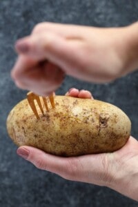 A person holding a potato with a fork, preparing crock pot baked potatoes.