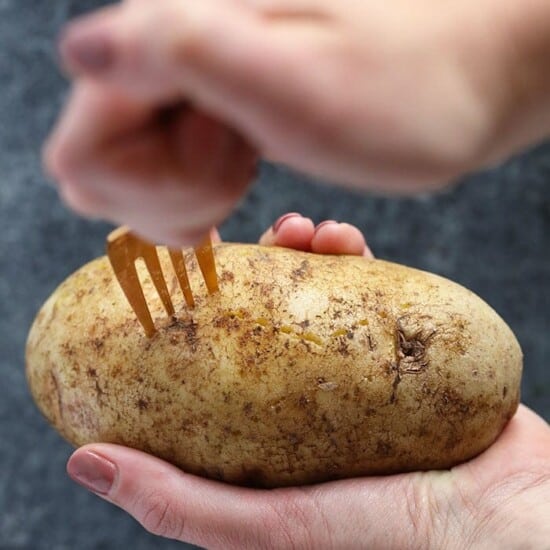 A person holding a potato with a fork, preparing crock pot baked potatoes.