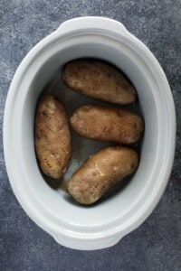 Crock pot baked potatoes served in a white bowl on a gray surface.